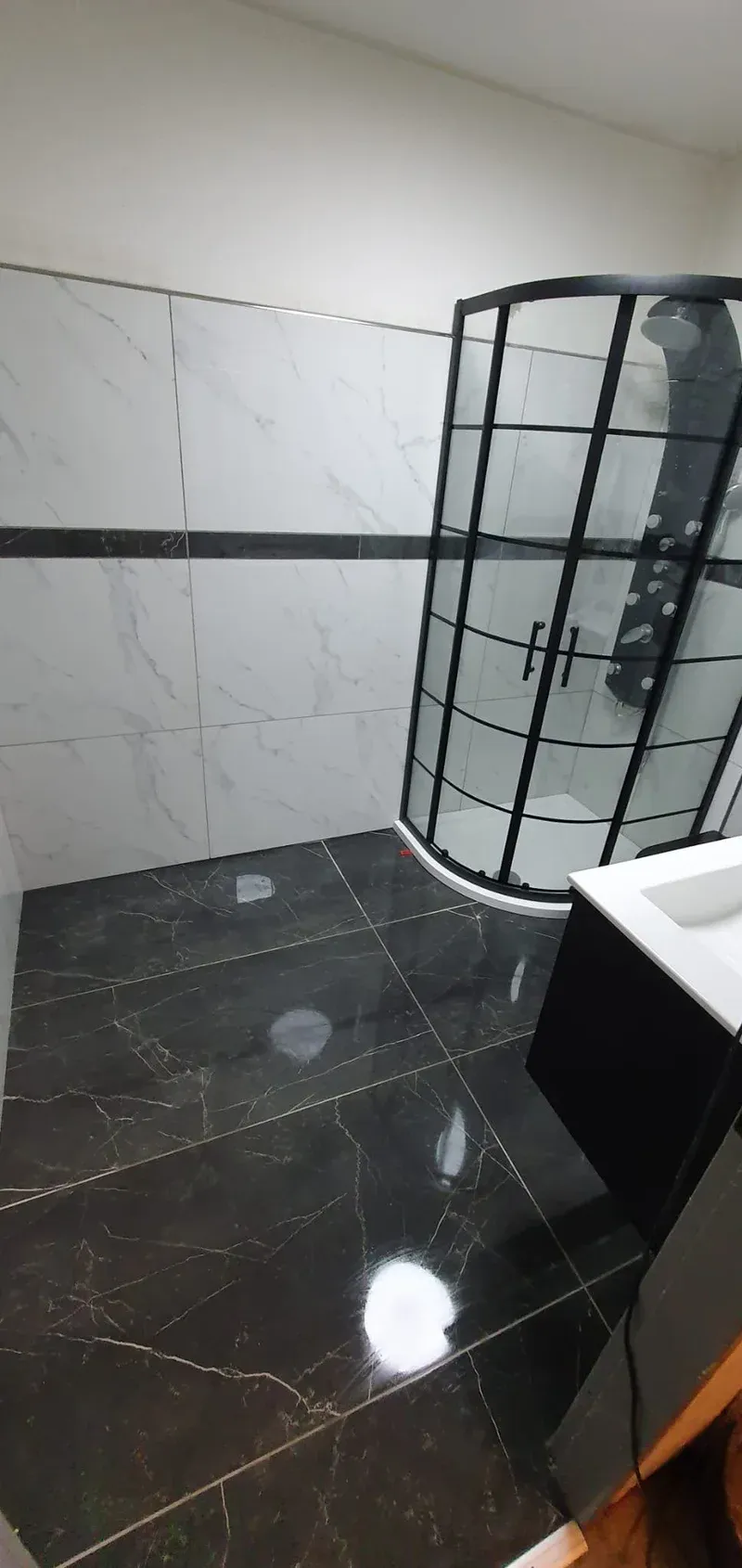 Dasselbe Bad fertig: Eckdusche, Waschtisch mit Spiegelschrank, Wände in Marmoroptik und dunkler Boden