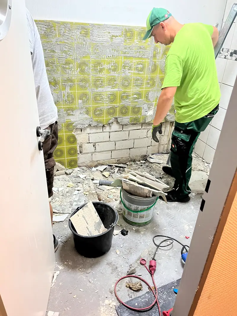 Handwerker stemmt die alten Wandfliesen im Bad ab